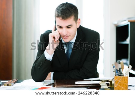 Happy caucasian businessman talking on mobile phone while sitting at his desk in the office