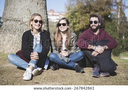 Group of friends two women and one man, sitting on floor in the park