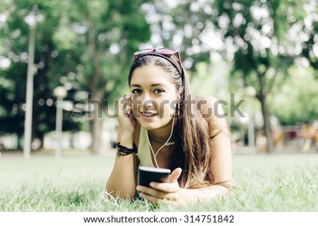Beautiful young woman lying on the grass in a park with a smart phone listening to music