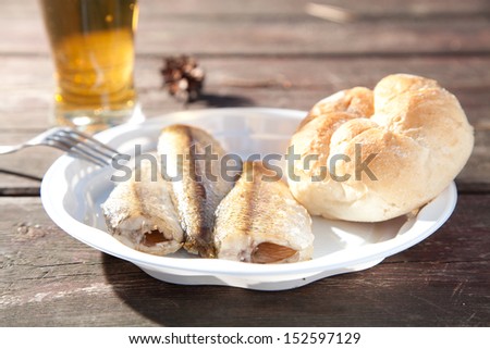 Fried fish on a plastic plate in the woods on a bench and drinking beer