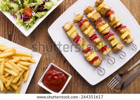 Grilled chicken skewers with pineapple, peppers and onions served with french fries and vegetable salad