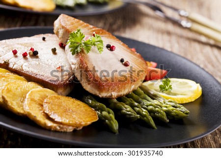 Grilled tuna steak served on asparagus with roasted zmieniakami on a black plate.