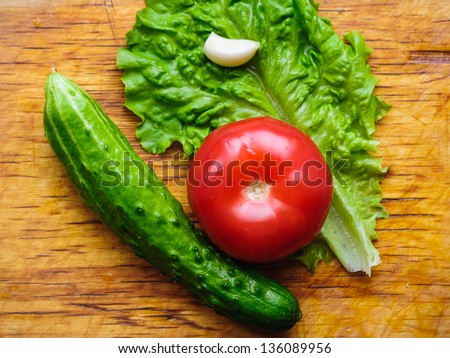Fresh vegetables for salad - tomato, cucumber, salad leaf and garlic on a wooden plate