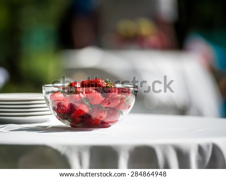 A glass bowl of fresh red juicy strawberries on a table served outdoor for wedding ceremony