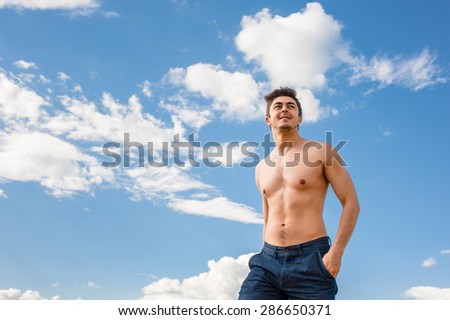 Fit handsome healthy athletic young happy man with bare torso enjoying life under scenic blue sky on sunny day. Concept of recreation, healthy lifestyle and well being.