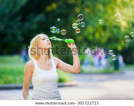 Happy young beautiful blonde woman enjoys her weekend having fun with soap bubbles in the park. Concept of leisure and fun