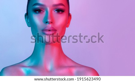 High fashion model metal silver lips and face woman in colorful bright neon UV blue and purple lights, posing in studio, beautiful girl, glowing makeup, colorful makeup. Glitter Bright Neon Makeup