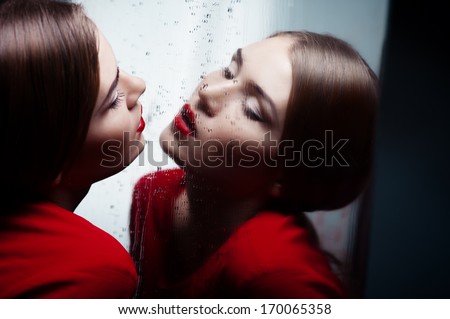 Beautiful sexy girl in red with bright makeup looks in the mirror