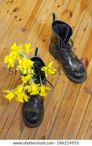 Black military muddy shoes with yellow narcissus on wooden floor near concrete wall