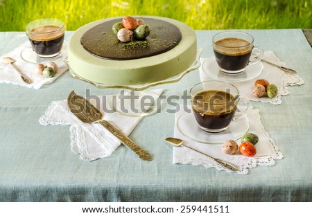 Easter table with tea matcha cheesecake and black coffee on background of green grass. Near sweet-stuff eggs. From series elegant desserts