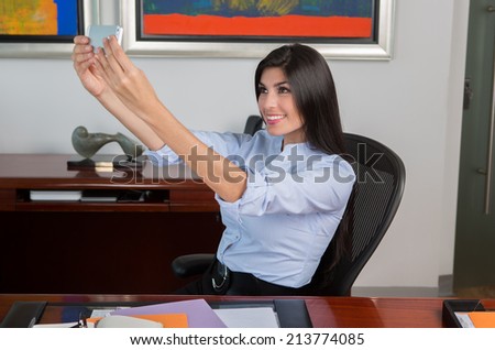 Smiling business woman taking photo using cell phone in office