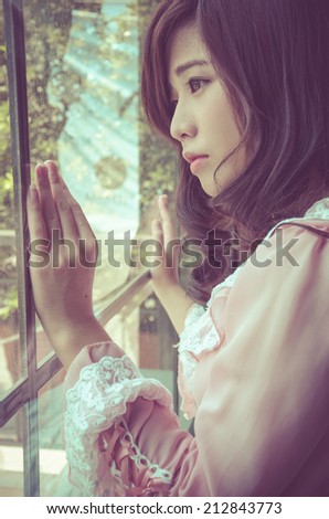 Vintage beautiful woman in pink dress looking through the window, warm tone
