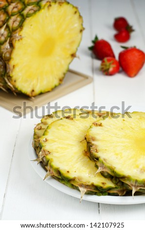 Slices of pineapple on white plate with strawberries in the background