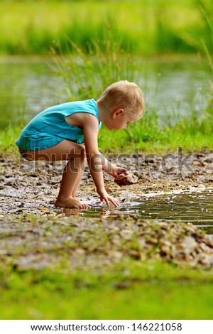 The boy on the shore of the lake, blonde playing with water and stone on a very beautiful nature, the water, the baby in water