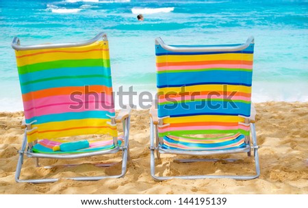 Two colorful beach chairs under by the ocean with sunscreen, with couple in the ocean