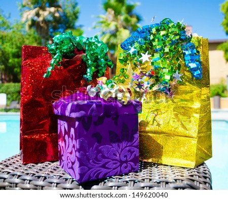 red and gold Gift bags and purple gift box with ribbon by the swimming pool with palm trees on background