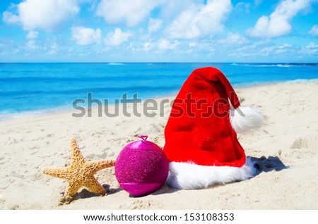 Christmas hat with christmas ball and starfish on the beach by the ocean - holiday concept