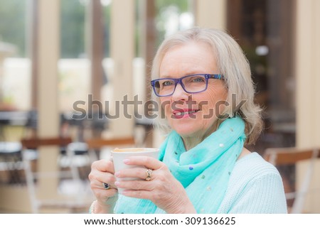 Beautiful blonde middle aged lady sits at cafe with coffee drink