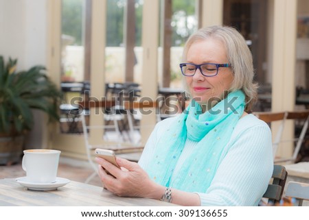 Middle aged woman sits at cafe texting or operating her smart cell phone