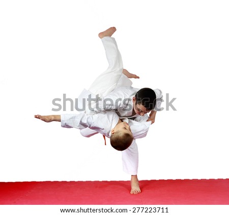 On a red mat athletes are training judo throws