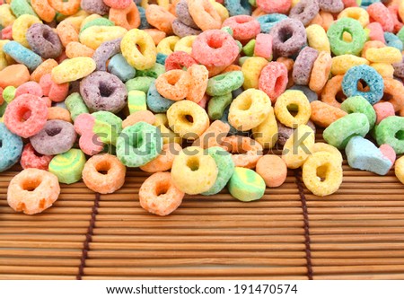 Delicious and nutritious fruit cereal loops flavorful on white background, healthy and funny addition to kids breakfast on bamboo mat