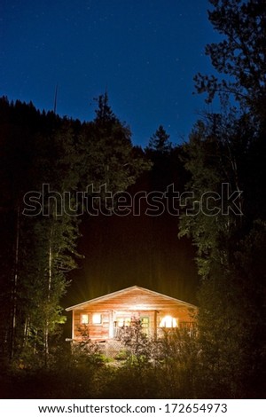 Cabin lit up with the night sky in the back ground.