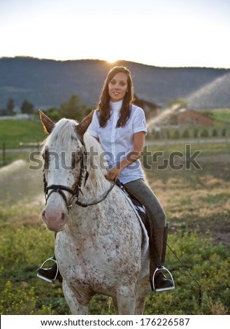 Attractive, well dressed woman sitting on a horse with the sun setting behind her.