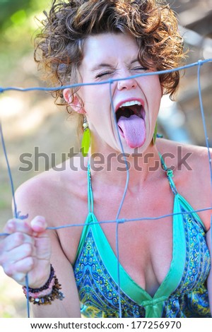 Attractive woman with a low cut, green dress screaming through a wire fence.