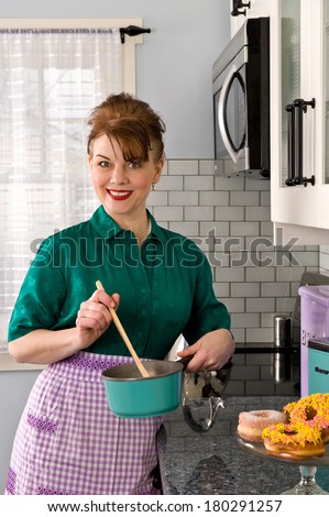 An attractive middle-aged woman in a kitchen wearing a vintage dress and a purple apron, stirring a pot a green pot with a wooden spoon