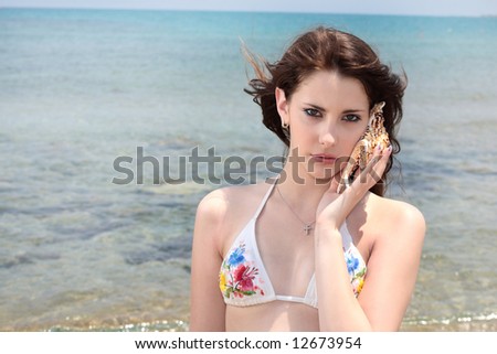 beautiful teen girl in swimwear holding up a shell against sea background