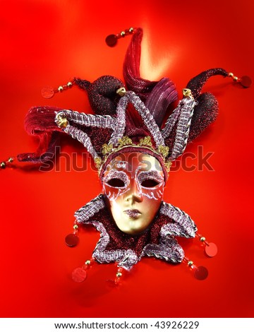 Ornate carnival mask over red metallic background.