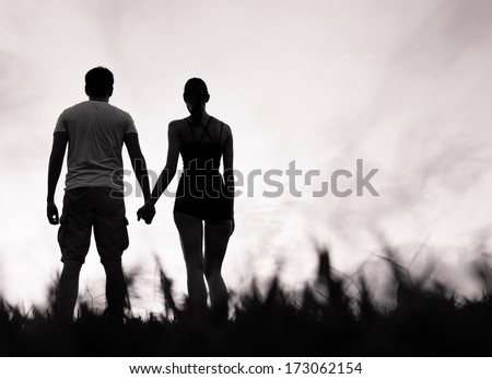 Silhouette of happy couple holding hands looking in the sunset