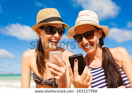Girls using smart phone on the beach. Technology and beach concept. Summer holiday
