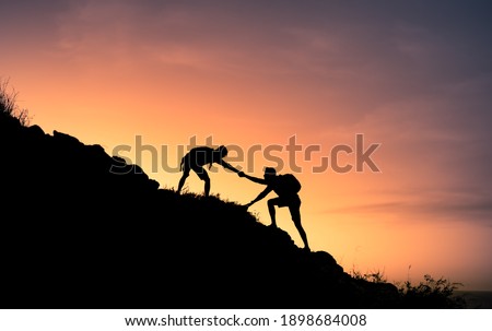 Two male hikers helping each other climb up a mountain. Teamwork and perseverance. 