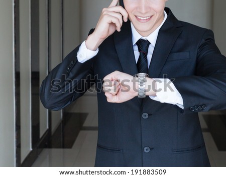 Business man on the phone while checking the time on his wrist watch.