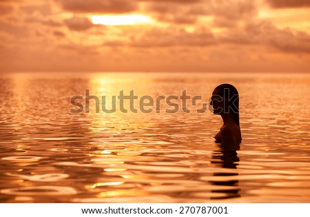 Surreal setting of woman in the water at sunset. (location Hawaii)