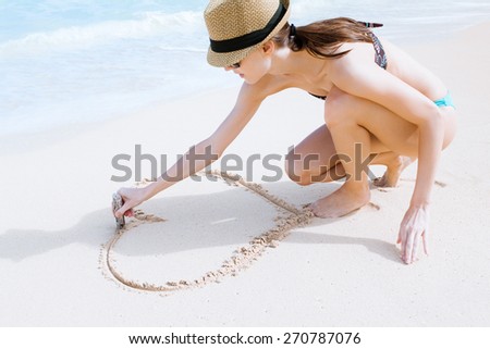 Woman drawing heart in the sand.  (love, travel concept)