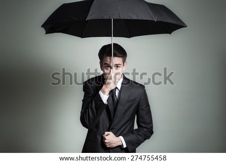 Business man making worried face while holding on tight to and umbrella.