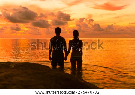 Couple holding hands in the water while watching the sunset.