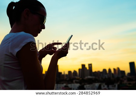 Silhouette of woman in the city using her mobile device.