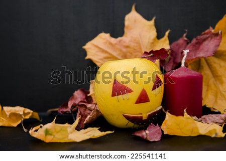 apples with faces for Halloween surrounded by autumn leaves and candles