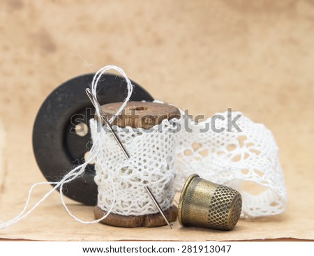 white lace ribbon, wound on a wooden bobbin with needle for sewing, a large black wooden button and a metal thimble, vintage, vintage accessories