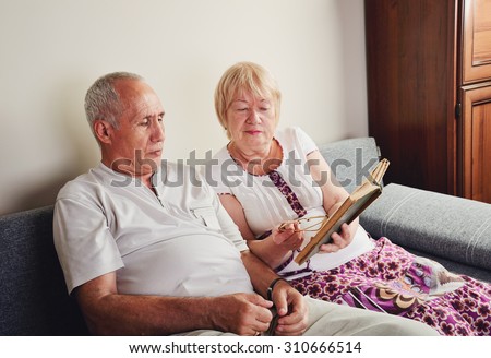 older man and woman 60-65 years old sitting on the sofa and reading a book. horizontal