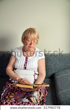 elderly woman reading a book sitting on the couch vertical format