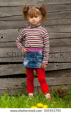 Beautiful little five-year girl posing for the camera outdoor near wooden wall