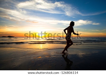 Silhouette of a young woman jogger at sunset on the seashore.