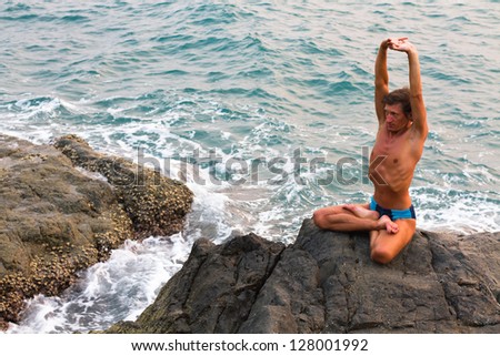 Young man doing yoga exercise in the lotus position on the deserted wild stone sea beach
