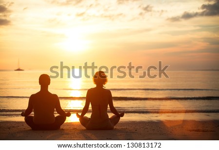 A young couple sitting on the beach of the sea in the lotus position at sunset, yoga practice