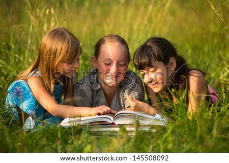 Portrait of cute kids reading book in natural environment together.