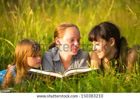 Three little sister reading book in natural environment together